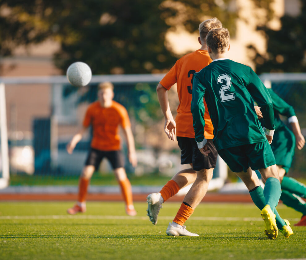 Soccer football players kick a ball towards a goal during a match in the soccer stadium. Youth football teams in a game. Footballers in action on the tournament game. Adult football competition
