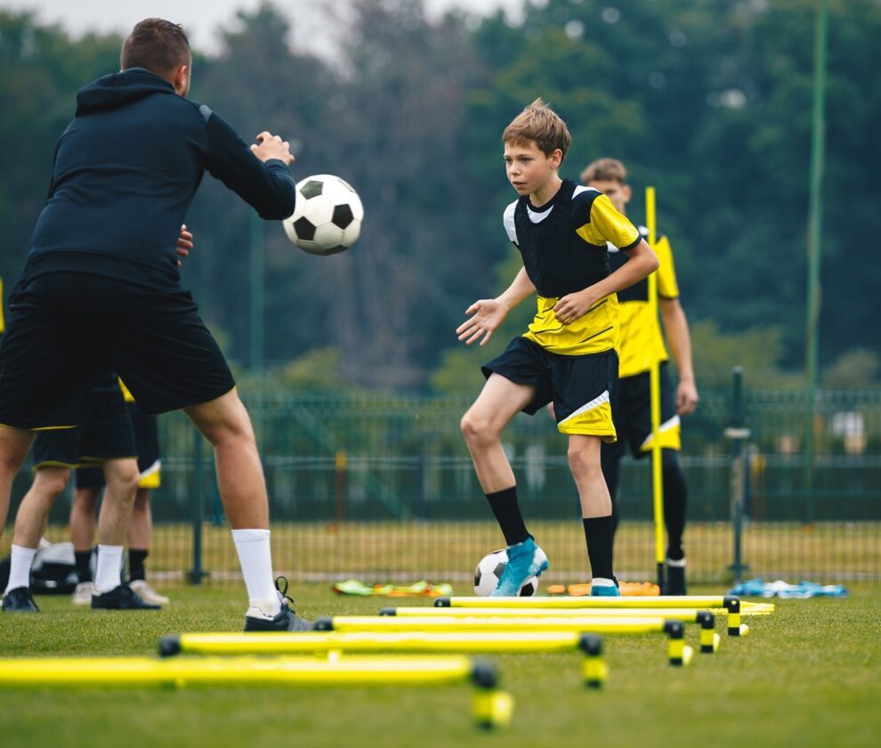 Teenagers on soccer training camp. Boys practice football with young coaches. Junior level athletes improving soccer skills on outdoor training. Player kick soccer ball to coach and ladder skipping